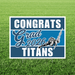 Blue and white yard sign with "CONGRATS Grad 2026 TITANS" text and an illustration of a Native American mascot holding a spear, mounted on green grass.