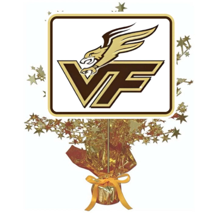 Gold and brown VF logo with winged eagle on rectangular sign mounted on gold foil-wrapped centerpiece base with gold ribbon bow and scattered star decorations.