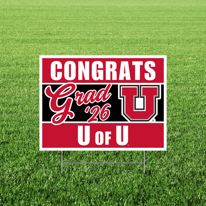 Red and white University of Utah yard sign with "CONGRATS Grad '26 U OF U" text and the Utes logo, displayed on grass.