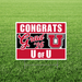 Red and white University of Utah yard sign with "CONGRATS Grad '26 U OF U" text and the Utes logo, displayed on grass.