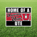 University of Utah yard sign with red and black horizontal stripes, large white "U" logo, and text reading "Home of a University of Utah Ute" displayed on green grass.