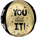 Cream-colored foil balloon with black text reading "YOU did IT!" surrounded by stars and decorative dots, with black curved panel on the side.