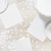 White luncheon napkins arranged on a light wood surface with decorative white confetti, displaying the folded napkins and plates in a flat lay composition.