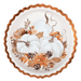 Round white paper plate with a scalloped copper rim featuring illustrated white pumpkins surrounded by autumn leaves and berries in orange and brown tones.