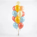 Bunch of 16 pastel balloons in cream, yellow, coral pink, and light blue arranged vertically with curled ribbons and a silver weight at the base.