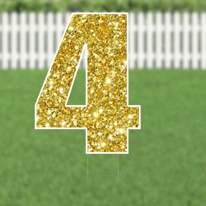 Gold glitter number 4 yard sign with white border and metal stakes, displayed on green grass with white picket fence background.