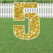 Gold glitter yard sign shaped like the number 5 with white border and metal stakes, displayed on green grass with white picket fence background.