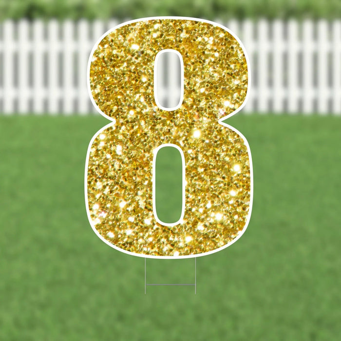 Gold glitter number 8 yard sign with white outline and metal stakes, displayed on green lawn with white fence background.