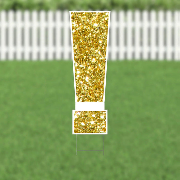Gold glitter exclamation point yard sign with white border and metal stakes displayed on green grass with white picket fence in background.
