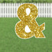 Gold glitter ampersand symbol yard sign with white border and stake legs displayed on a green lawn.