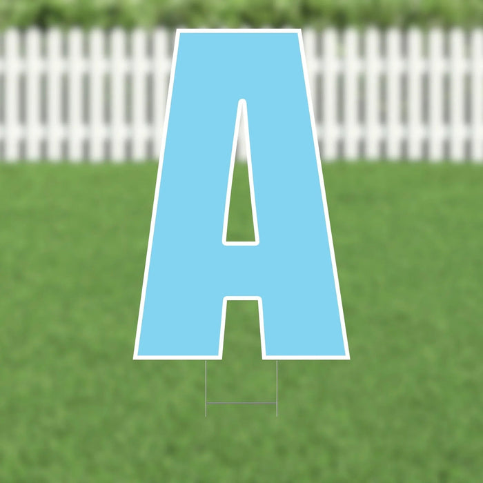 Light blue letter A yard sign with white outline and two support stakes, displayed on green grass with a white picket fence in the background.