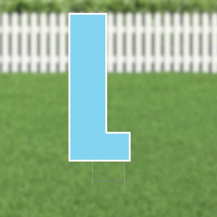 Light blue letter L yard sign with white border and metal stakes, displayed on grass with white picket fence in background.