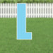 Light blue letter L yard sign with white border and metal stakes, displayed on grass with white picket fence in background.