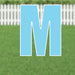 Large blue letter M yard sign with white border and metal stakes, displayed on green grass with white fence background.