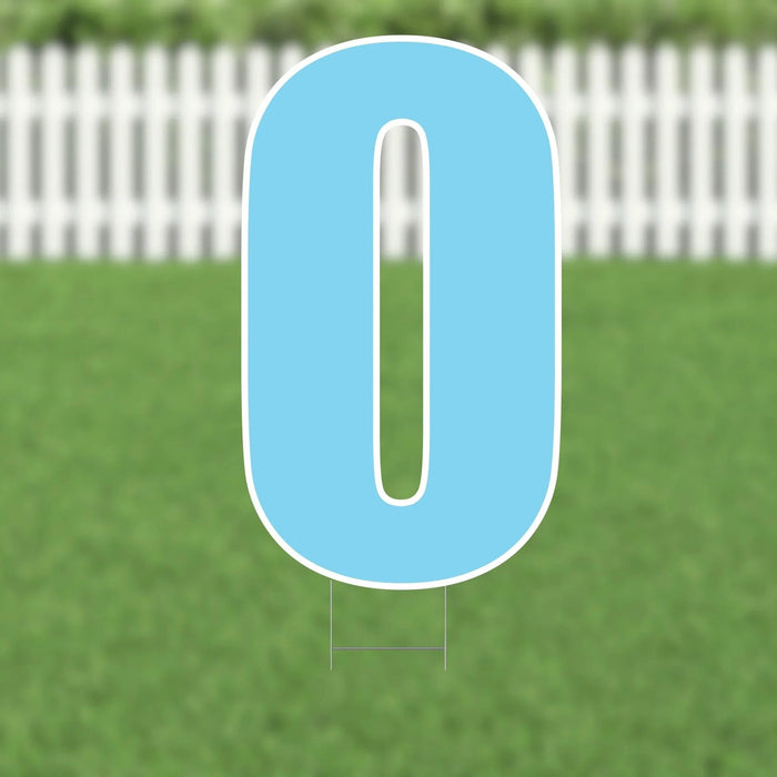 Light blue yard card letter O with white outline and mounting stakes, displayed on grass with a white picket fence in the background.