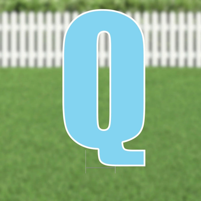 Light blue letter Q yard card with white outline and base, displayed against a white picket fence and green grass background.