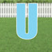 Large blue letter U yard sign with white border and metal ground stakes, displayed on green grass with white picket fence backdrop.