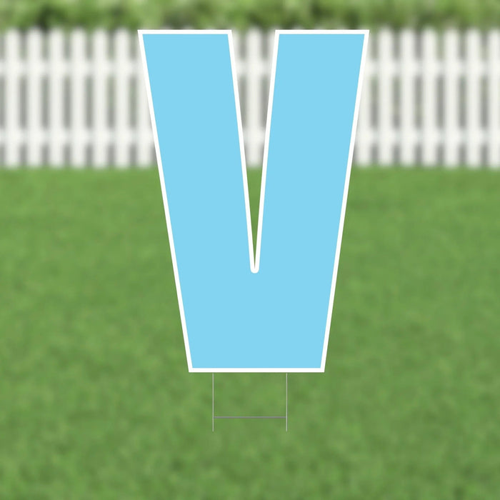 Large light blue letter V yard sign with white border and metal stakes, displayed on a residential lawn with white picket fence in background.