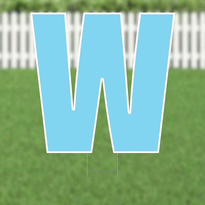 Large light blue letter W yard sign with white outline and metal stake, displayed on grass with white picket fence in background.