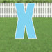 Bright blue capital letter X yard sign with white border and metal stakes, displayed on grass with white picket fence background.