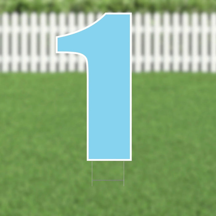 Light blue yard sign shaped like the number 1 with white border and metal stakes, displayed on a grass lawn with white picket fence in background.
