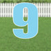 Large light blue yard sign displaying the number 9 with white outline, mounted on two metal stakes against a residential lawn and white picket fence background.