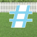 Light blue yard sign with white striped hashtag symbol displayed on green grass with white picket fence in background.