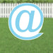 Light blue yard sign with a white @ symbol inside a circle, displayed on grass with a white picket fence in the background.