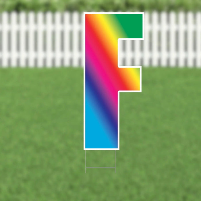Colorful yard card letter G with a rainbow gradient fill and white outline, displayed on a lawn with white picket fence background.
