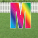 Colorful gradient yard card letter N with vibrant rainbow colors transitioning from blue to pink to yellow, displayed on green grass with white picket fence background.