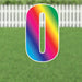 Colorful yard card letter P with a rainbow gradient transitioning through pink, red, orange, yellow, green, cyan, and blue, displayed on green grass with a white picket fence background.