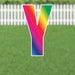 Colorful letter Y yard sign with rainbow gradient transitioning from pink and orange at the top through yellow, green, and blue to purple at the bottom, displayed on grass with a white picket fence background.