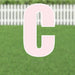 Large pink letter C yard sign with white outline displayed in grass with white picket fence in background.