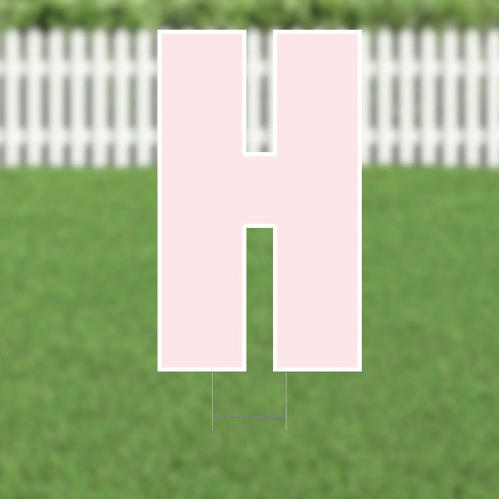 Pink yard card letter H displayed against a green lawn backdrop with a white picket fence.