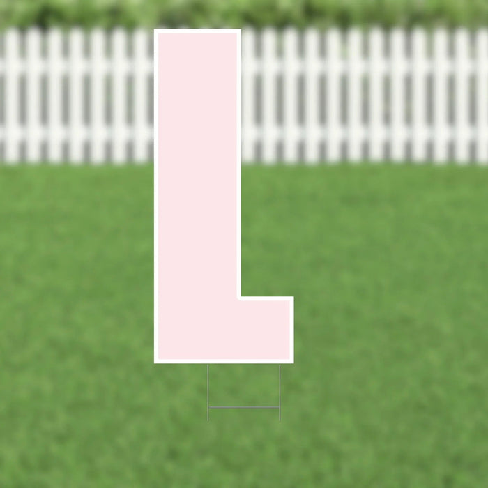 Pink letter L yard sign with white border and metal stakes displayed on a grass lawn with white picket fence background.