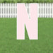 Large pink letter N yard sign with white border and metal stakes, displayed on green grass with white picket fence in background.