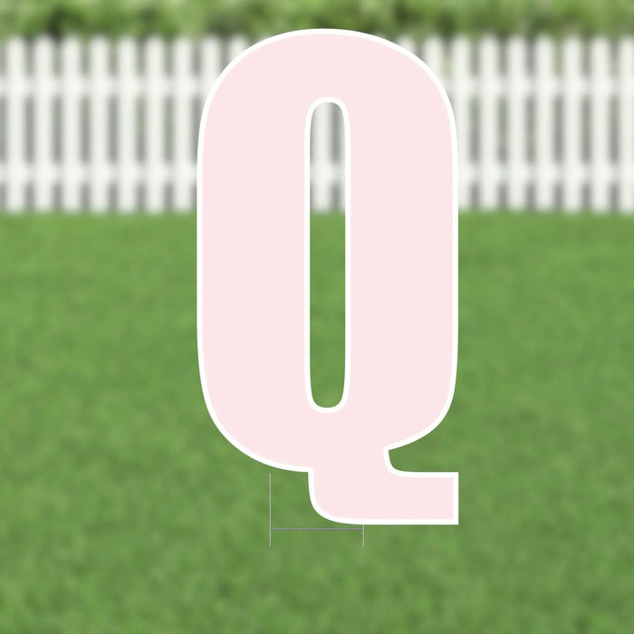 Large pink letter Q yard sign with white outline, approximately 21.5 inches tall, displayed on green grass with a white picket fence in the background.