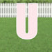 Pink letter U yard sign with white border and metal stakes, displayed on green grass with white picket fence in background.