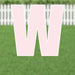 Large pink letter W yard sign with white border and metal stakes, displayed on grass with white picket fence in background.