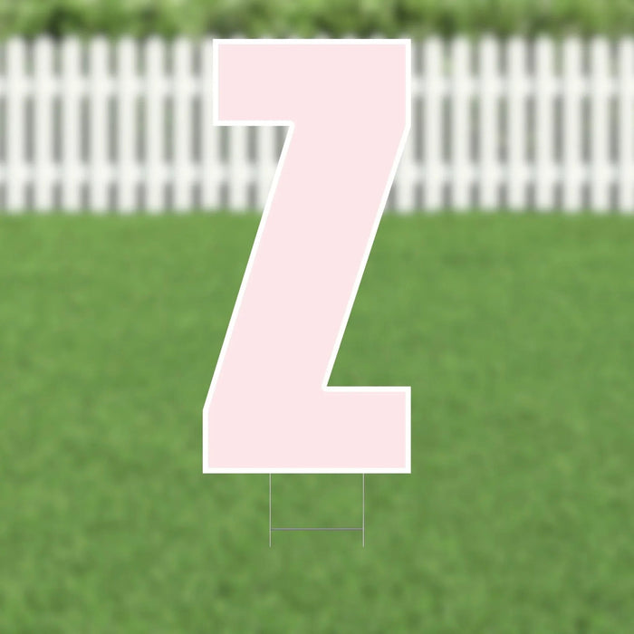 Pink yard card shaped like the letter Z with white outline and metal stakes, displayed on a green lawn with white picket fence background.