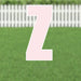 Pink yard card shaped like the letter Z with white outline and metal stakes, displayed on a green lawn with white picket fence background.