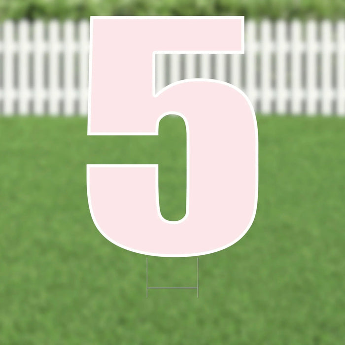 Pink yard card number 5 with white outline displayed on grass with white picket fence in background.