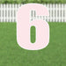 Large pink number 6 yard sign with white outline and metal stakes, displayed on green grass with white picket fence in background.