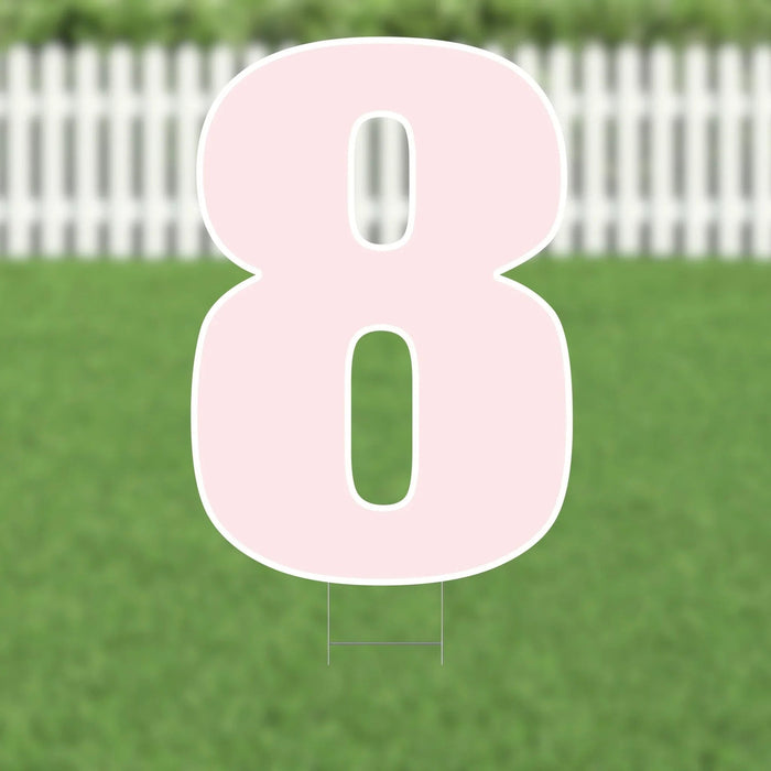 Pink number 8 yard sign with white border and metal stakes, displayed in a green lawn with white picket fence background.