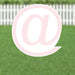 Large pink and white yard sign featuring an @ symbol, displayed on green grass with a white picket fence in the background.