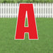 Large red letter A yard sign with white outline and cutout details, displayed on a grass lawn with white picket fence in background.