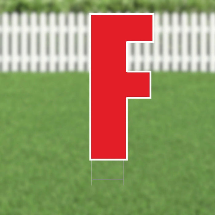 Red letter F yard sign with white border and metal stakes, displayed on green grass with white picket fence background.