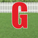 Red letter G yard sign with white outline and supporting stakes, displayed on a green lawn with white picket fence in background.