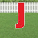 Red letter J yard sign with white border and metal stakes, displayed on a lawn with white picket fence in background.