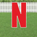 Large red letter N yard sign with white border and metal stakes, displayed on green grass with white picket fence background.